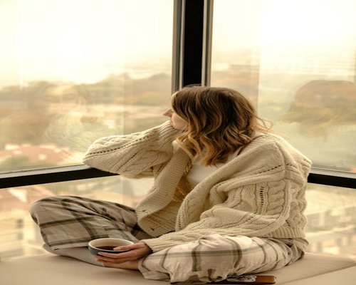 Serene woman in comfortable clothing meditation posture near a window with sunlight